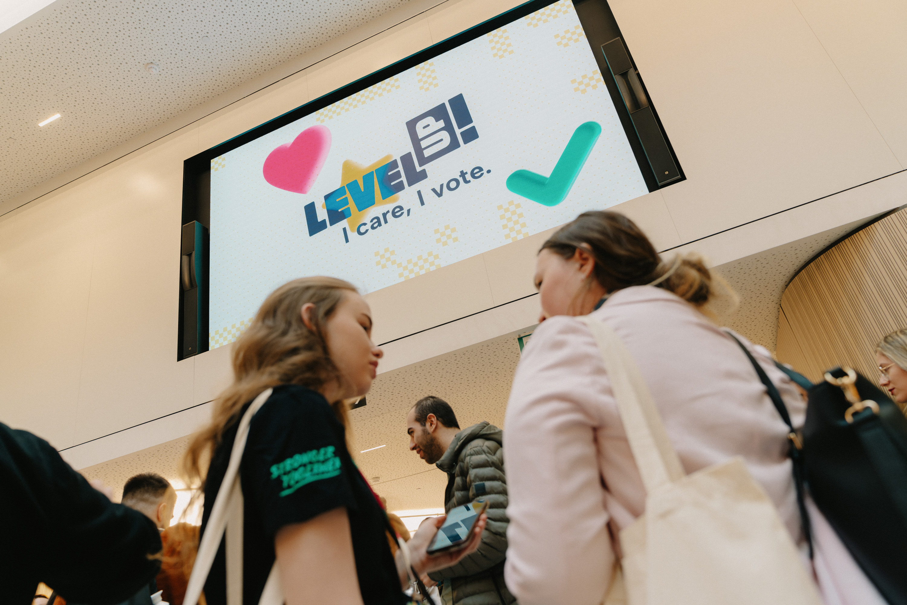 Two girls standing in front of a bog screen displaying the LevelUP! animated logo.